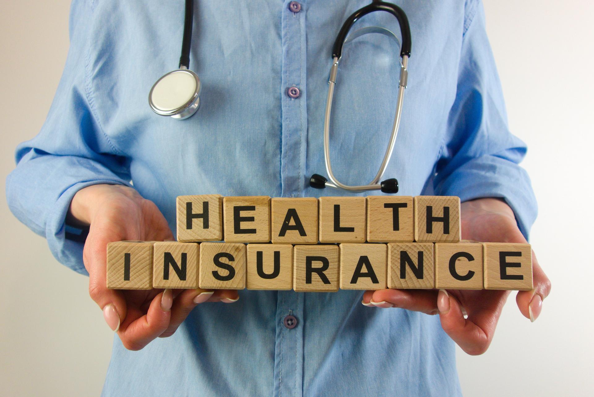 Female doctor holding text health insurance from wooden blocks